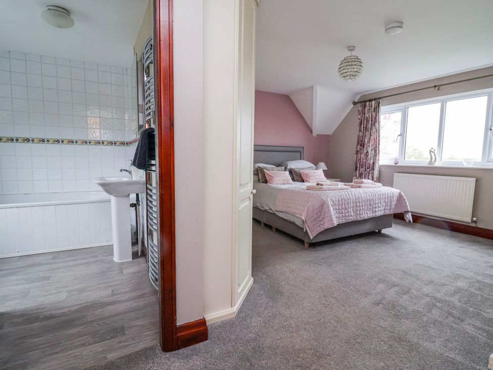 A bedroom with a bed and a bathroom featuring a bath and sink at Manor Wood in Farndon