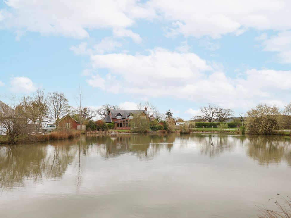 A house next to a pond with trees at Manor Wood in Farndon