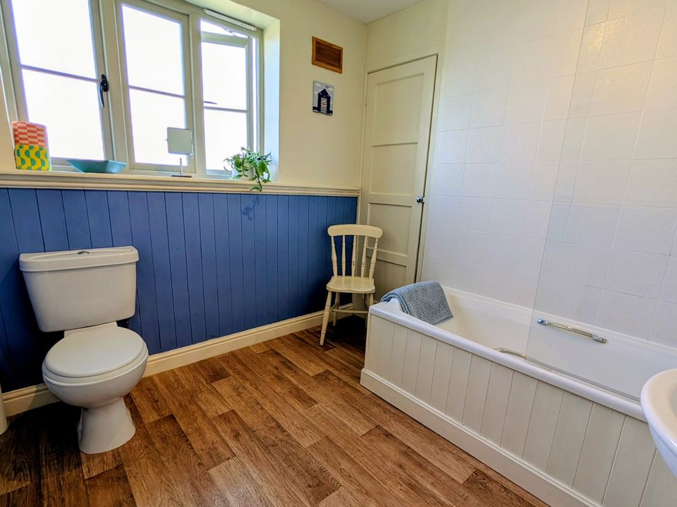 A bathroom with a toilet, bathtub, and chair at Beaconsfield Cottage in Briston
