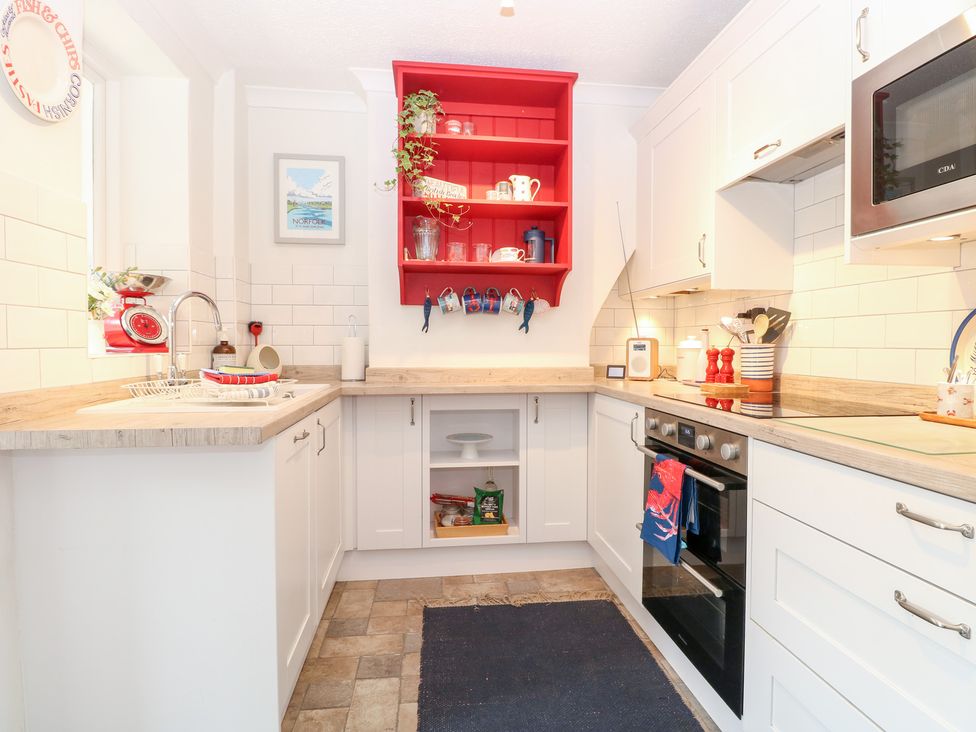 A kitchen with a red shelf and various kitchen items at Driftwood Cottage Heacham