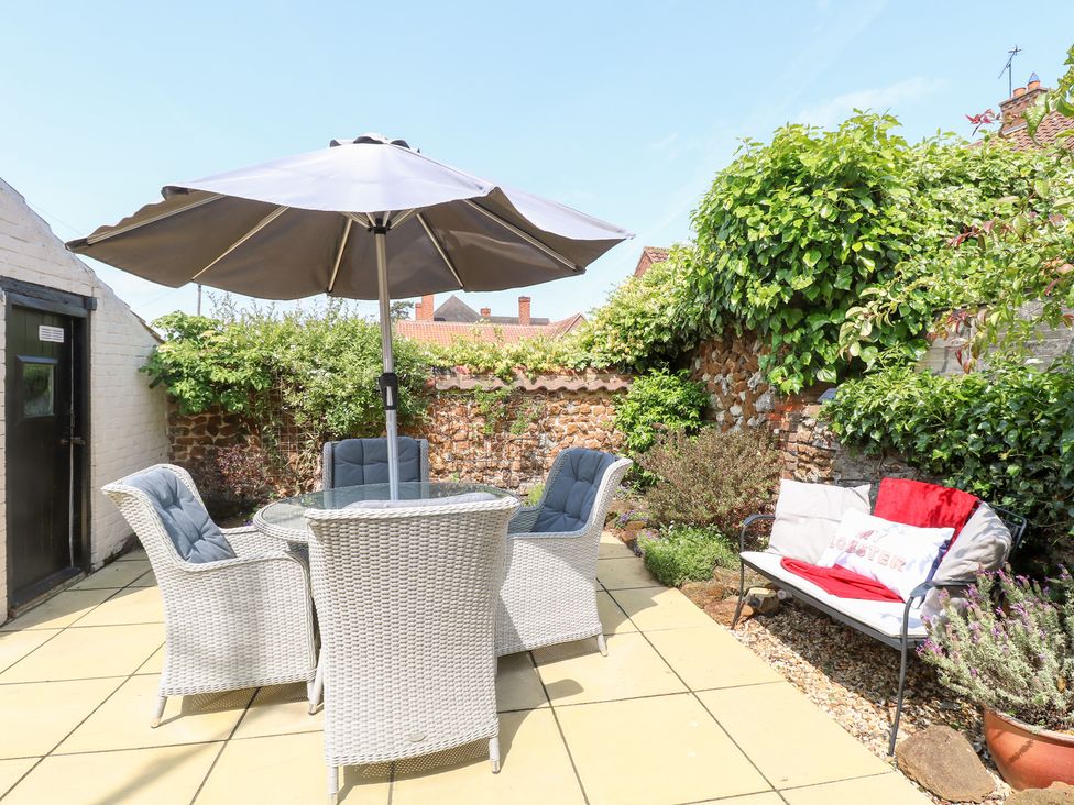 A garden with a table, chairs, and an umbrella at Driftwood Cottage in Heacham