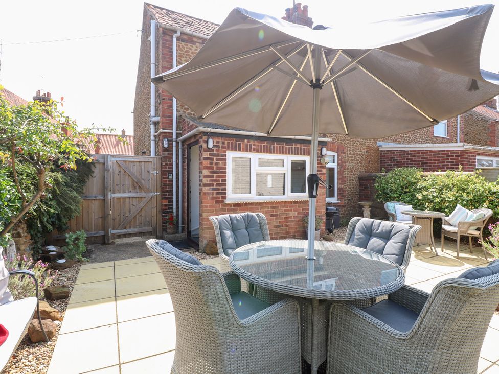A garden area with a table and chairs under an umbrella at Driftwood Cottage in Heacham