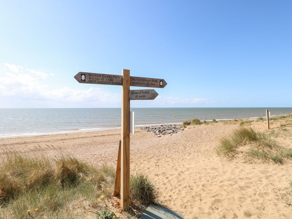 A beach with a signpost pointing to different paths at Driftwood Cottage in Heacham