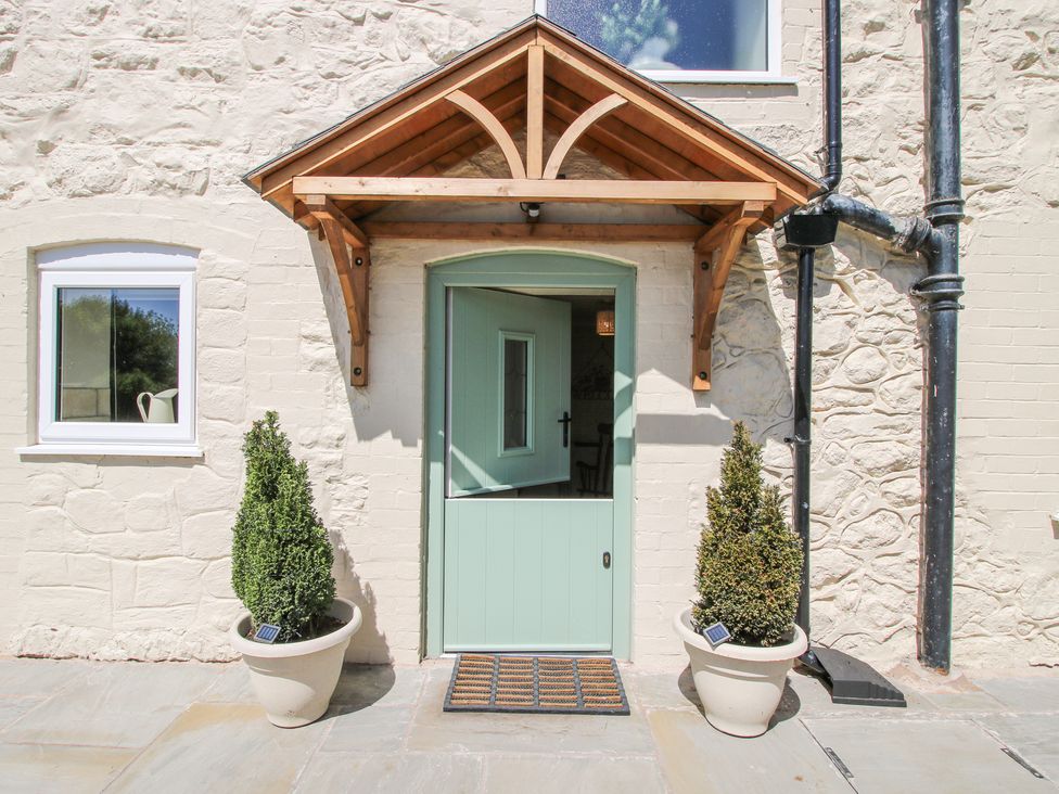 An exterior view of a half-glass door with a wooden canopy and two potted plants outside at Pennal Cottage in Maesbury Marsh near Knockin