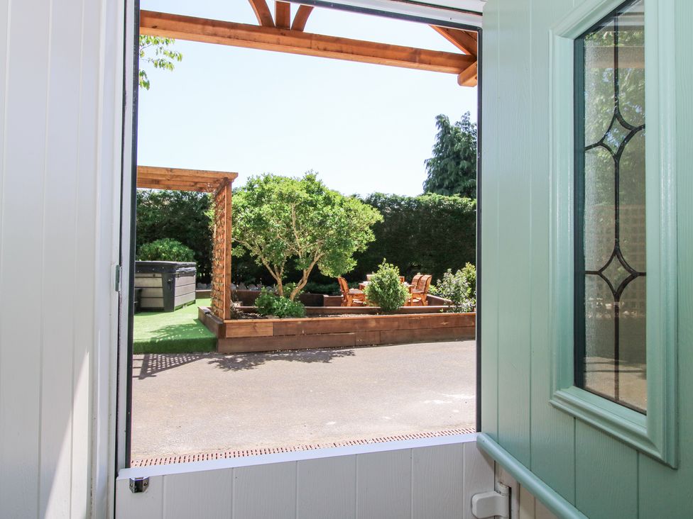 A view from an open door looking out to a garden with wooden planters trees and outdoor seating at Pennal Cottage in Maesbury Marsh near Knockin