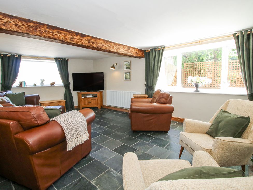 A living room with leather sofas a TV on a wooden stand and large windows with green curtains at Pennal Cottage Maesbury Marsh near Knockin