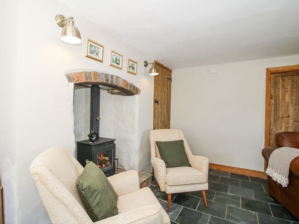 A sitting area with two beige armchairs and a wood stove under a brick arch at Pennal Cottage Maesbury Marsh near Knockin