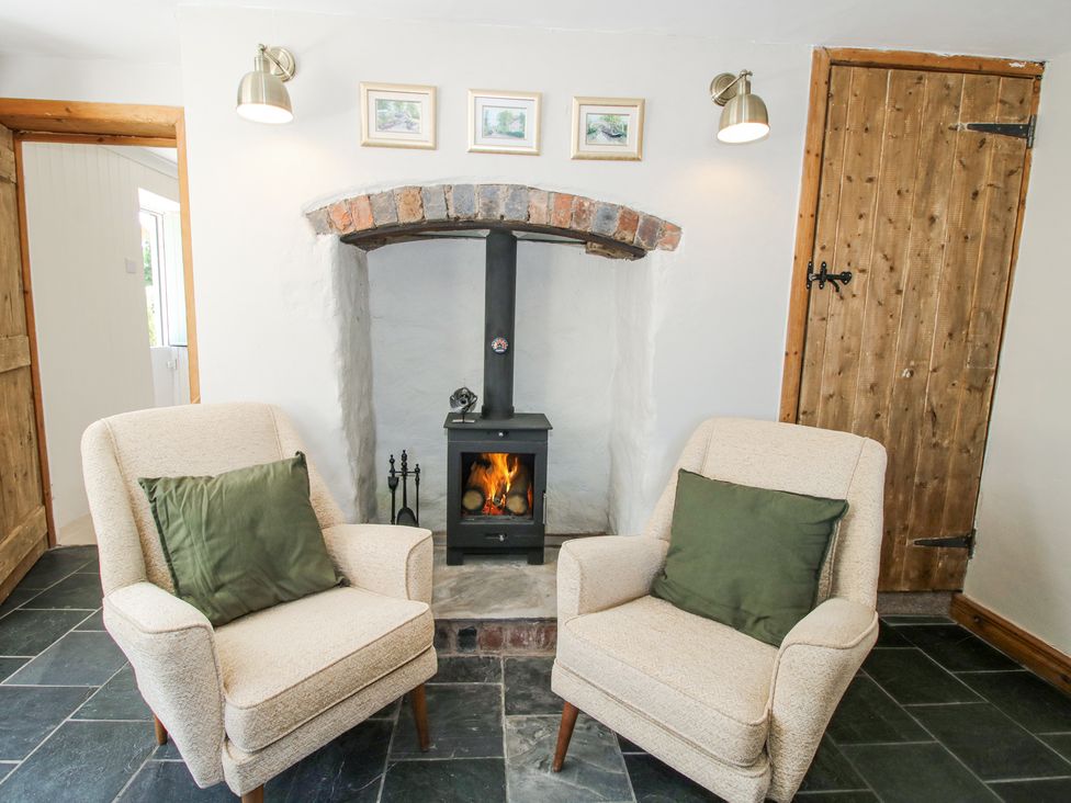 A sitting area with two upholstered armchairs and a wood burning stove in a white wall recess at Pennal Cottage in Maesbury Marsh near Knockin