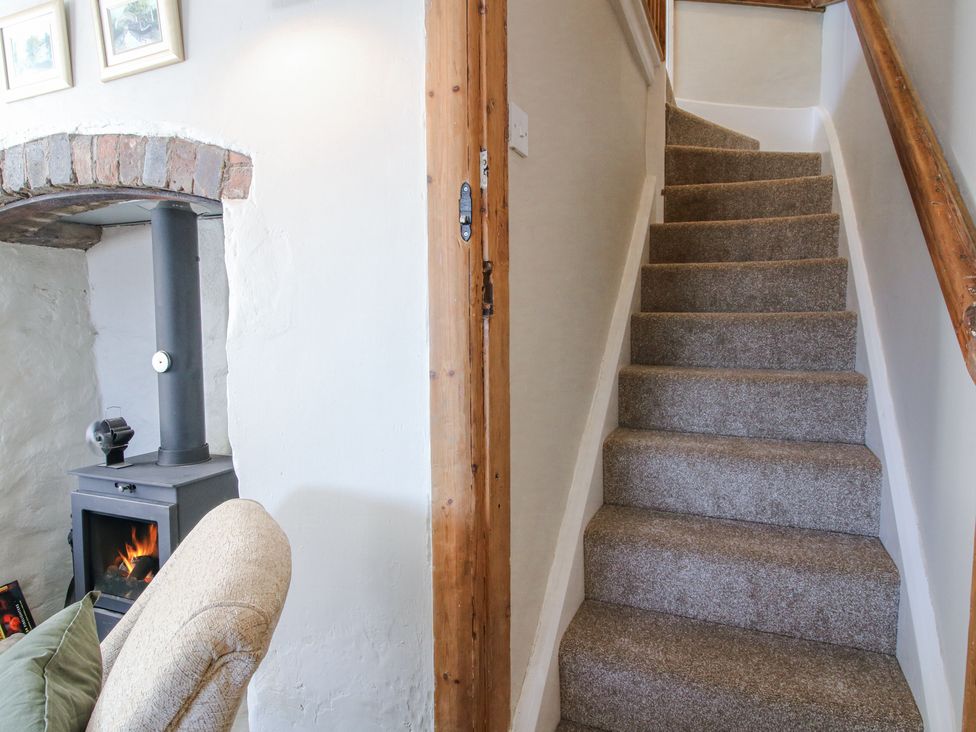 Carpeted stairs with wooden handrail next to a wall with fireplace and armchair at Pennal Cottage Maesbury Marsh near Knockin