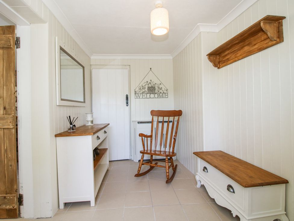 An entryway with a wooden rocking chair a white cabinet with a mirror and a white bench with wooden tops at Pennal Cottage in Maesbury Marsh near Knockin
