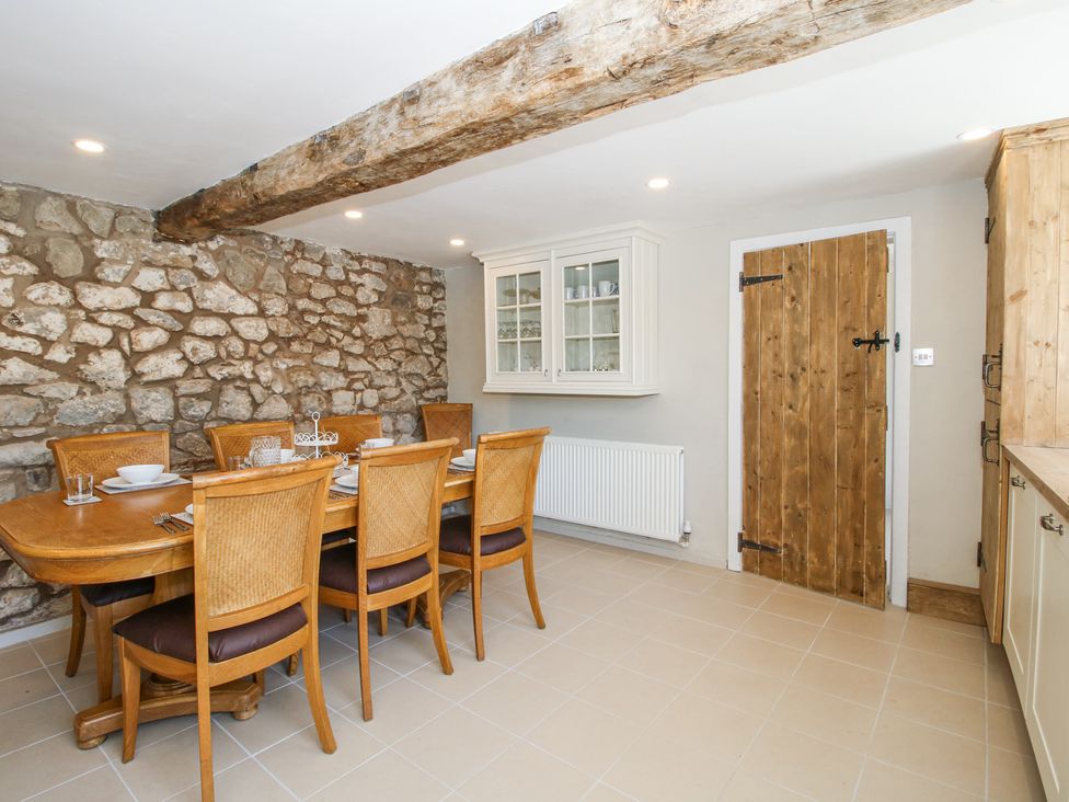 A dining room with a wooden table and six chairs a stone wall a wooden door and a white cabinet at Pennal Cottage Maesbury Marsh near Knockin