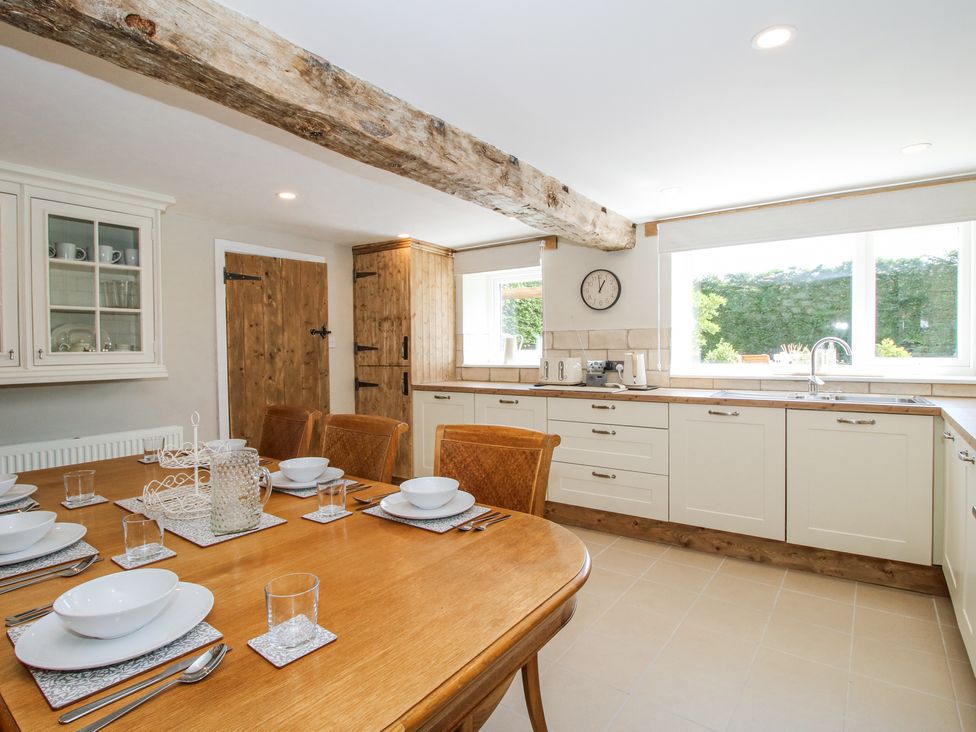 A kitchen with wooden dining table set for six and white cabinets with large window at Pennal Cottage in Maesbury Marsh near Knockin