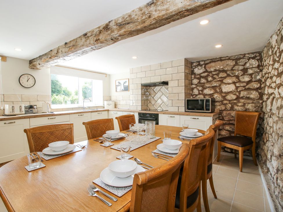 A kitchen with a dining table set for six and exposed stone walls at Pennal Cottage in Maesbury Marsh near Knockin