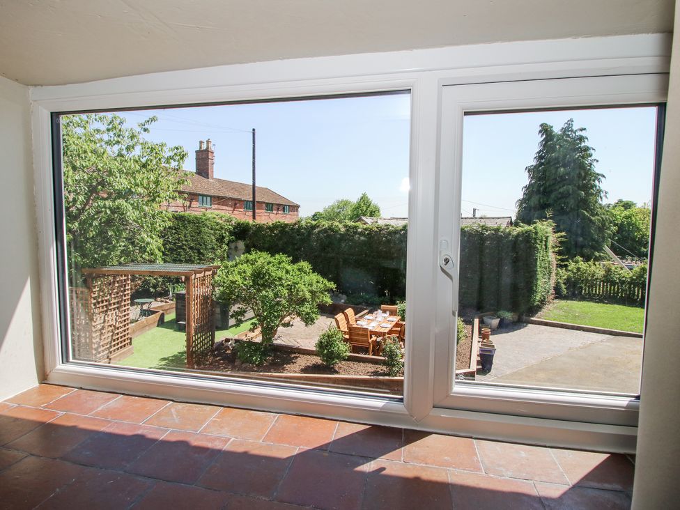 A view of a garden with outdoor dining table and chairs through a large window at Pennal Cottage in Maesbury Marsh near Knockin