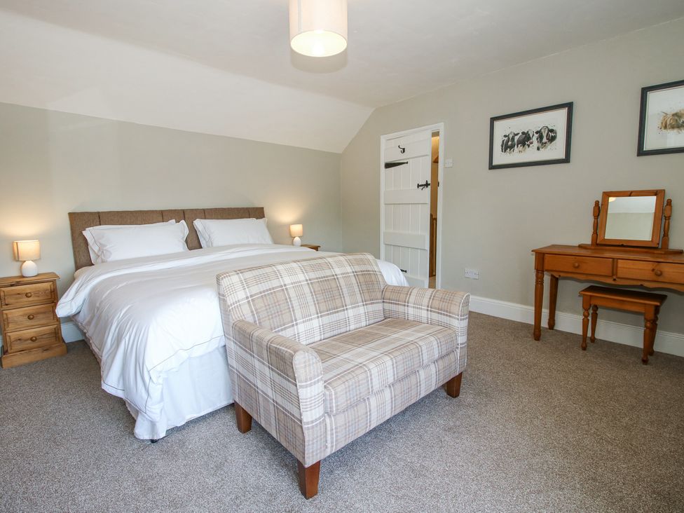 A bedroom with a bed two bedside tables a plaid upholstered bench a wooden dressing table and framed artwork at Pennal Cottage Maesbury Marsh near Knockin