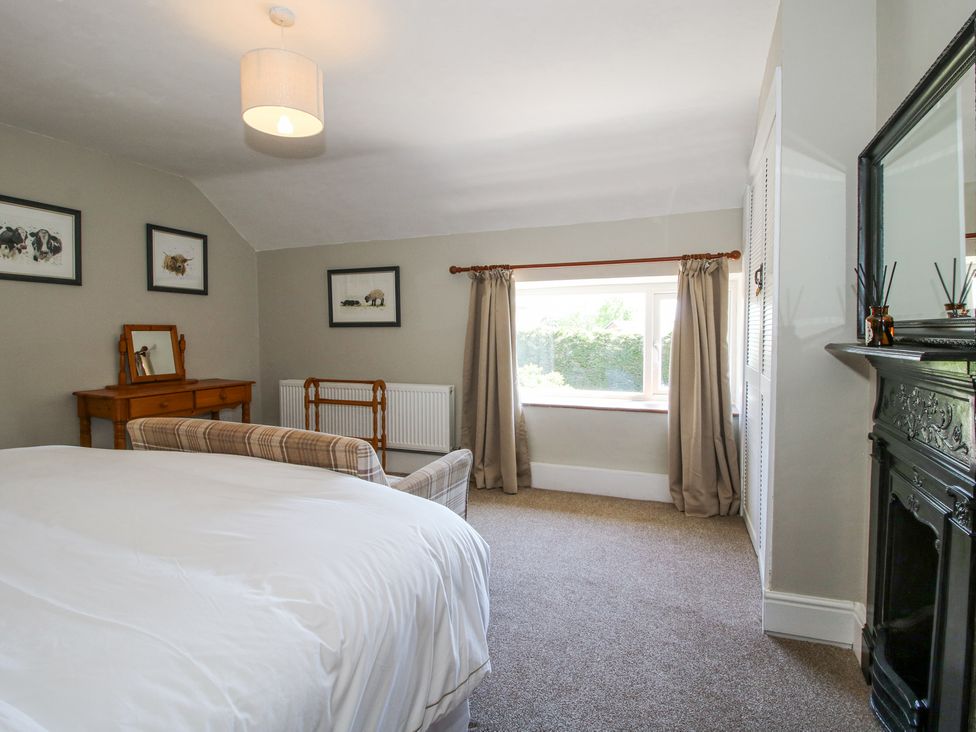 A bedroom with a bed a wooden vanity table a plaid armchair and a window with curtains at Pennal Cottage in Maesbury Marsh near Knockin