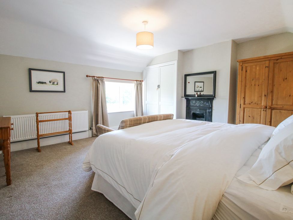 A bedroom with a bed, wardrobes, a window, and a fireplace at Pennal Cottage in Maesbury Marsh near Knockin
