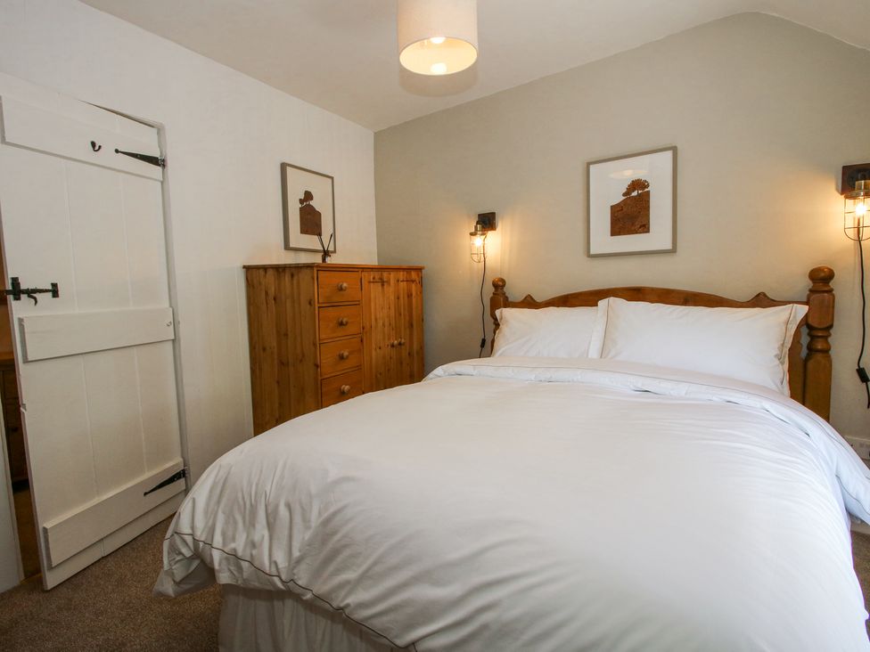 A bedroom with a wooden bed and white bedding a wooden dresser two framed pictures and wall lamps at Pennal Cottage in Maesbury Marsh near Knockin