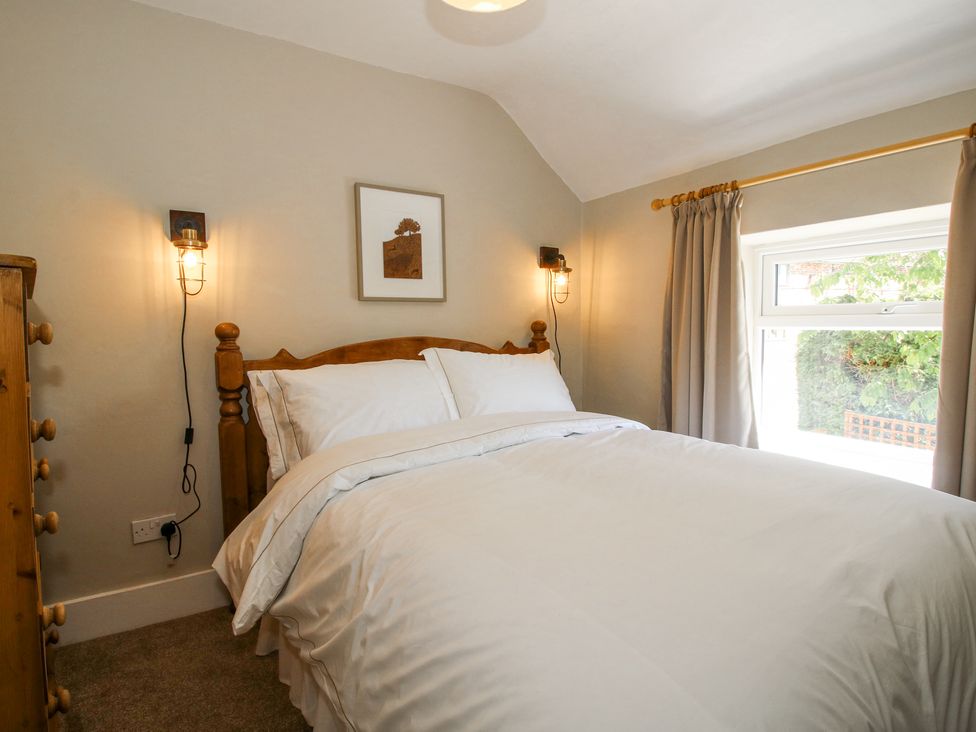 A bedroom with a wooden bed a dresser two wall lamps and a window with curtains at Pennal Cottage in Maesbury Marsh near Knockin