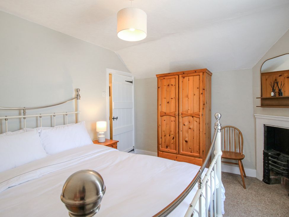 A bedroom with a metal bed frame a wooden wardrobe a wooden chair and a bedside table with a lamp at Pennal Cottage in Maesbury Marsh near Knockin