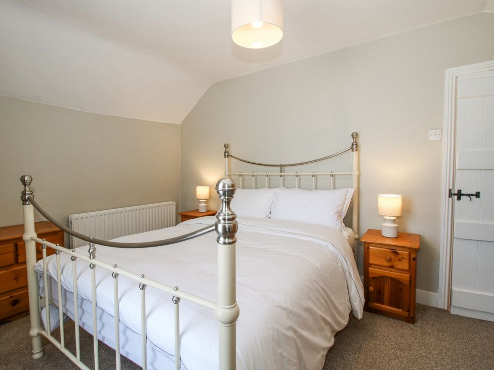 A bedroom with a metal bed frame white bedding two wooden bedside tables with lamps at Pennal Cottage Maesbury Marsh near Knockin