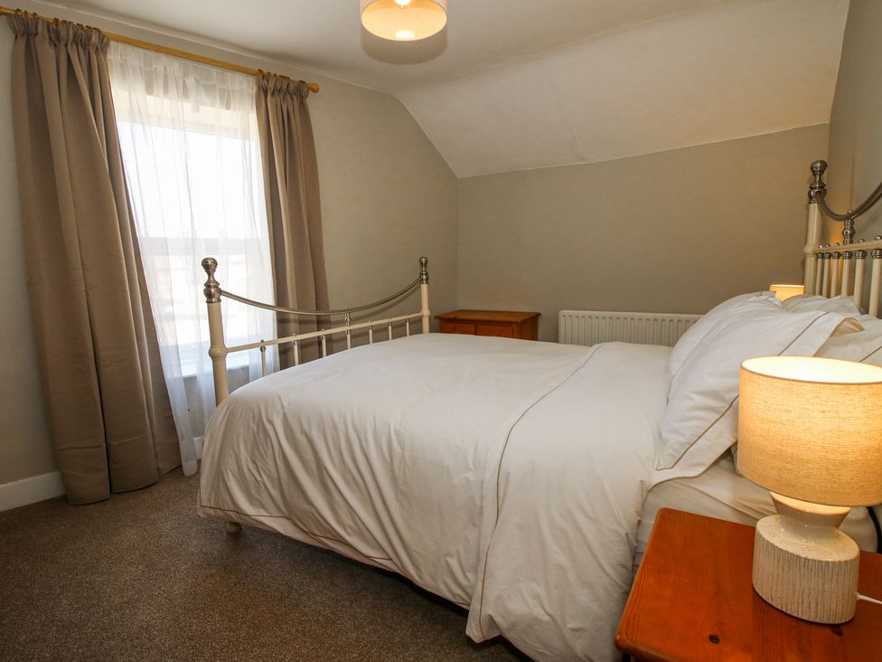 A bedroom with a metal bed frame white bedding bedside table with lamp wooden furniture and curtains at Pennal Cottage in Maesbury Marsh near Knockin