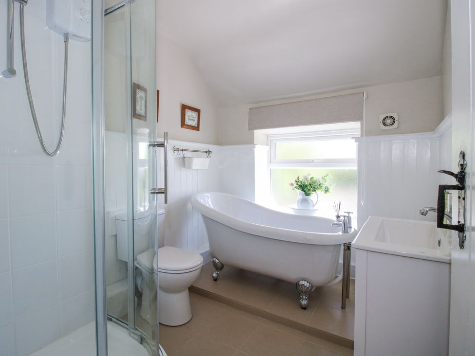 A bathroom with a shower enclosure toilet freestanding bathtub sink and a window with flowers at Pennal Cottage in Maesbury Marsh near Knockin