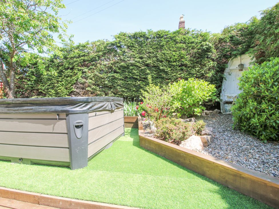 A garden area with an above ground hot tub surrounded by artificial grass and plants at Pennal Cottage in Maesbury Marsh near Knockin