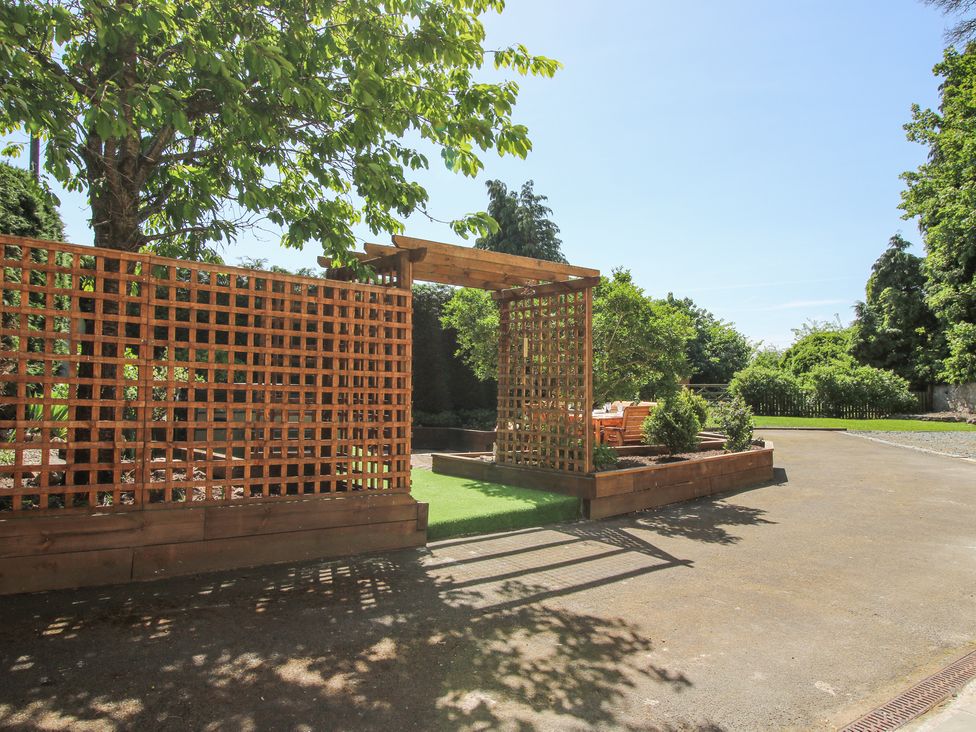 A wooden trellis structure with plants and outdoor seating in a garden at Pennal Cottage Maesbury Marsh near Knockin