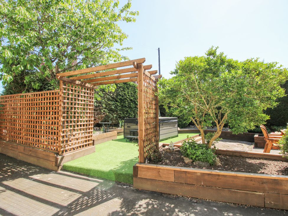 A garden with wooden trellis and pergola near seating area and small tree at Pennal Cottage in Maesbury Marsh near Knockin