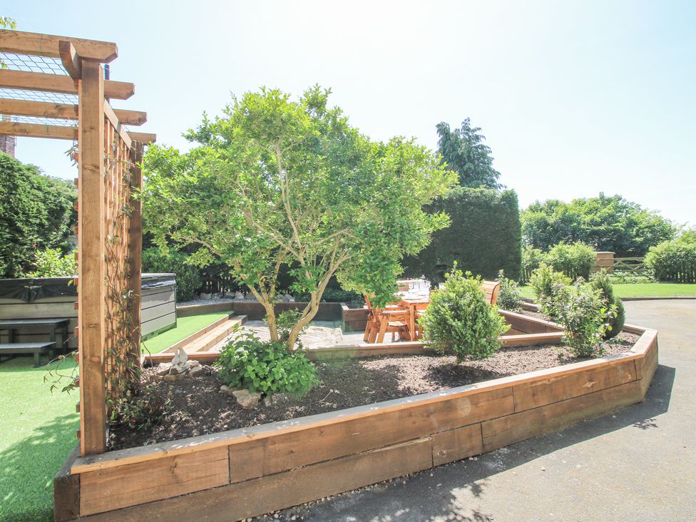 An outdoor garden area with a wooden raised planter, small trees, a wooden pergola, and a table with chairs at Pennal Cottage Maesbury Marsh near Knockin