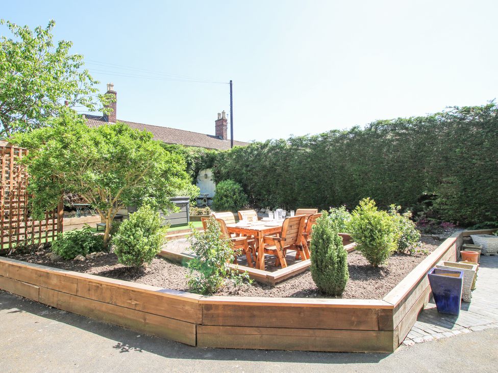 A garden area with wooden raised beds containing shrubs and a wooden dining table with chairs at Pennal Cottage Maesbury Marsh near Knockin