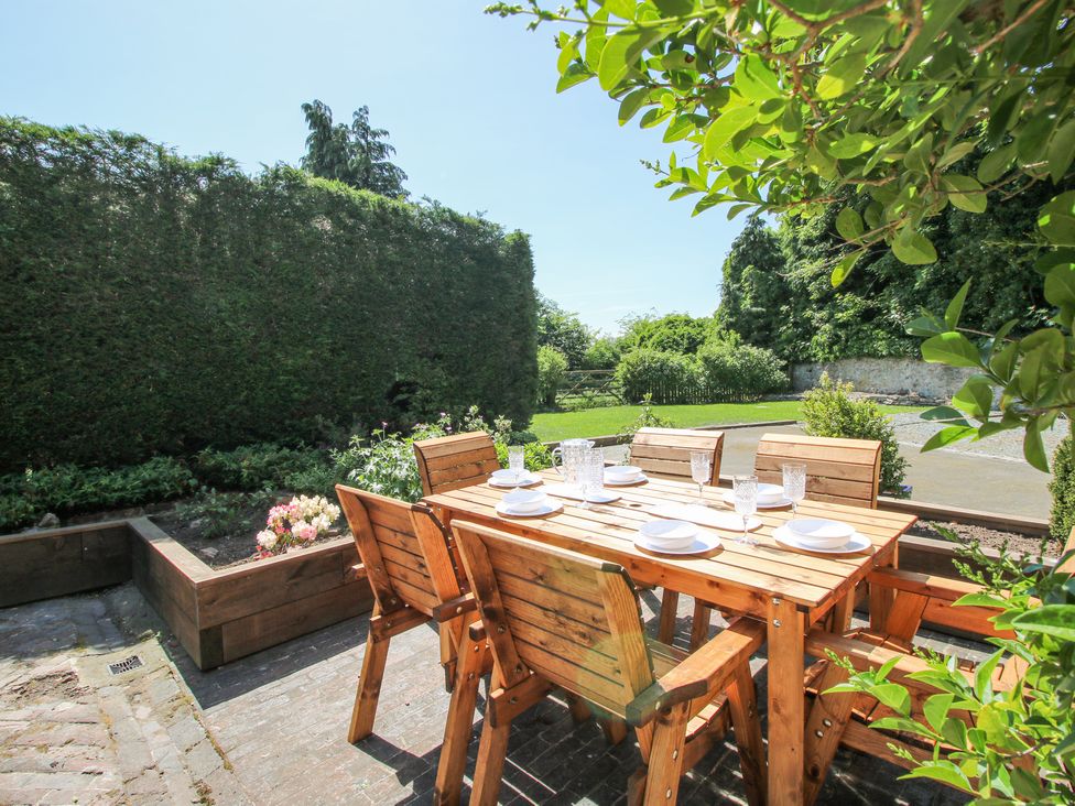An outdoor patio with a wooden dining table and six chairs set with plates and glasses at Pennal Cottage in Maesbury Marsh near Knockin