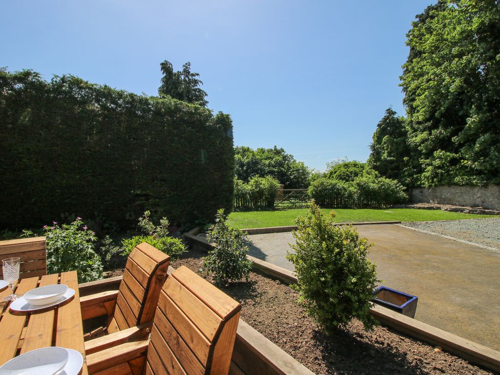A garden with wooden chairs and a table near hedges and a green lawn at Pennal Cottage in Maesbury Marsh near Knockin