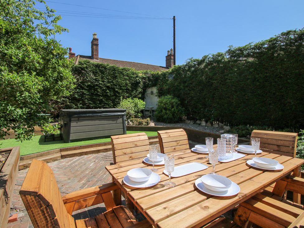 An outdoor patio with a wooden dining table and chairs set with plates and glasses at Pennal Cottage in Maesbury Marsh near Knockin