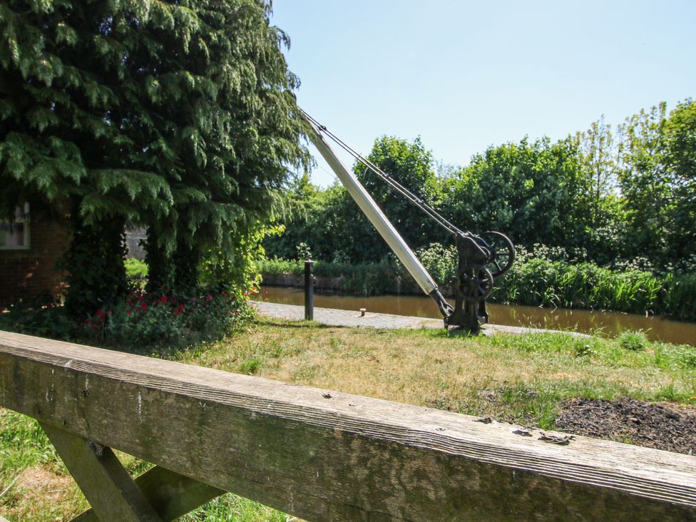 A canal with a mechanical gate mechanism and trees in the background at Pennal Cottage Maesbury Marsh near Knockin