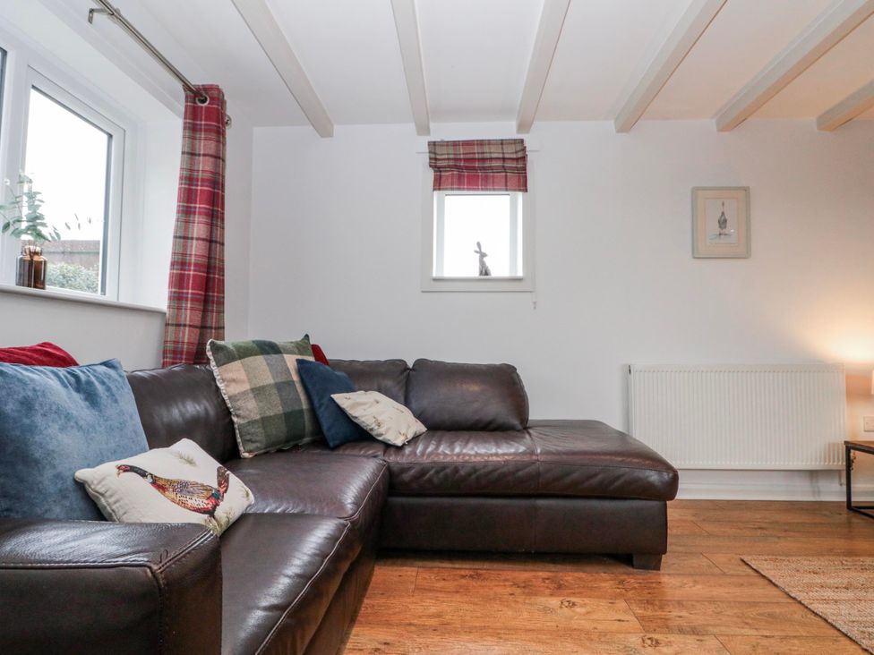 A living room with a leather sofa and cushions at Wold Cottage in Hunmanby