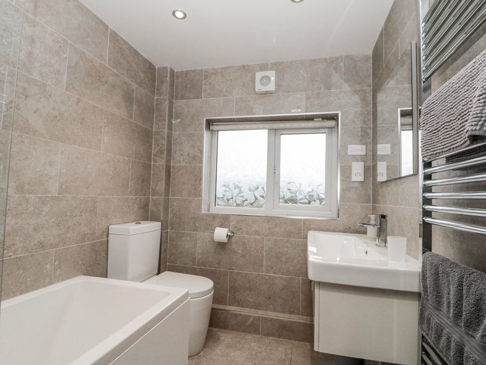 A bathroom with a bath tub toilet sink and window at Wold Cottage in Hunmanby