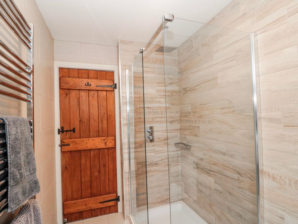 A shower area with a glass door and wooden door at Wold Cottage in Hunmanby
