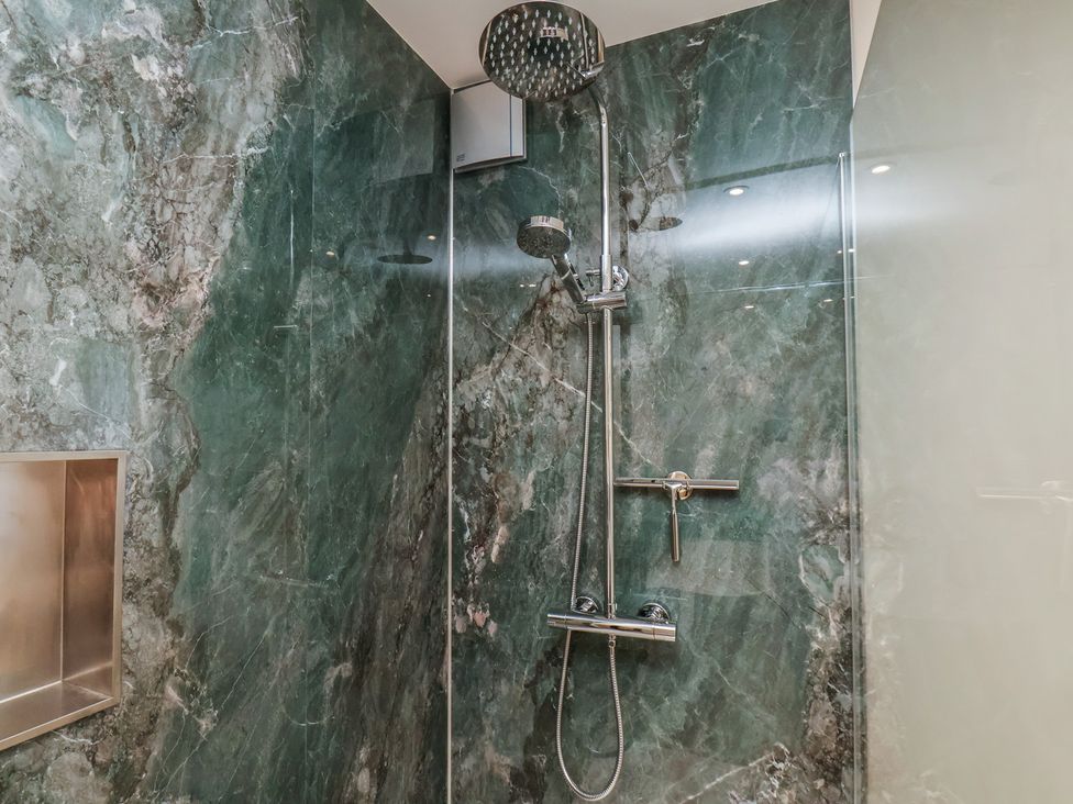 A shower with marble walls and a shower head at The Farmhouse in Boggle Hole near Robin Hood's Bay