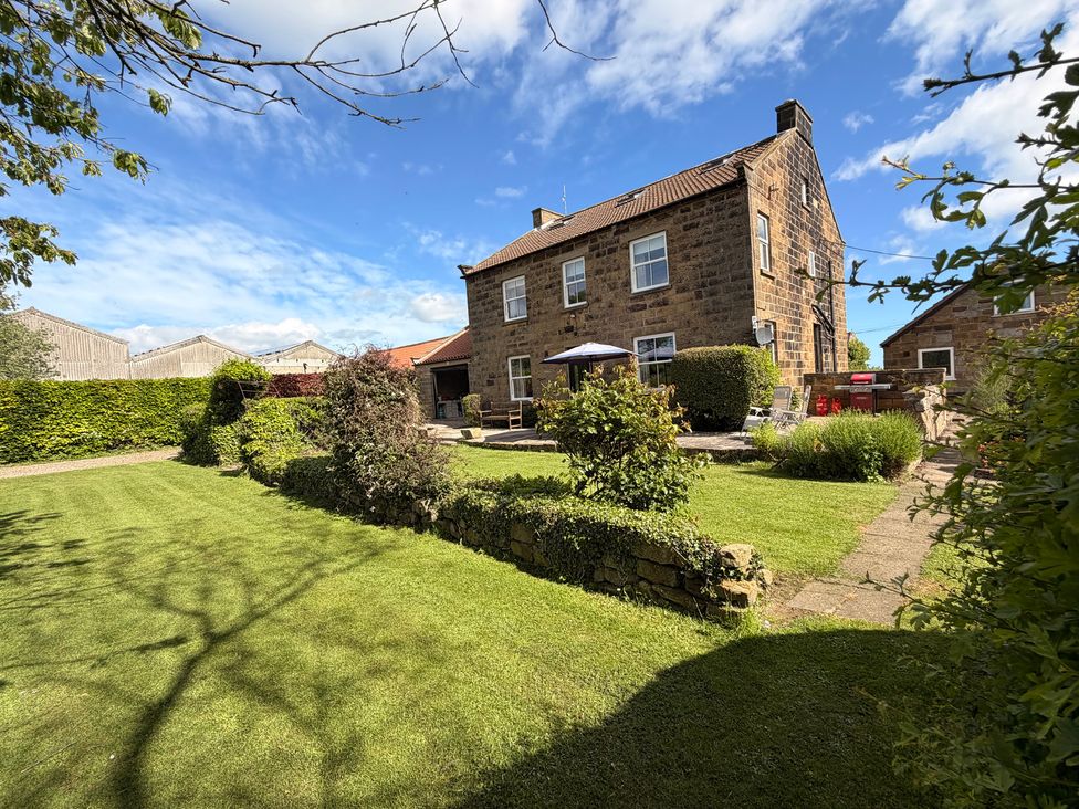 A garden with a house, seating and umbrella at The Farmhouse in Boggle Hole near Robin Hood's Bay