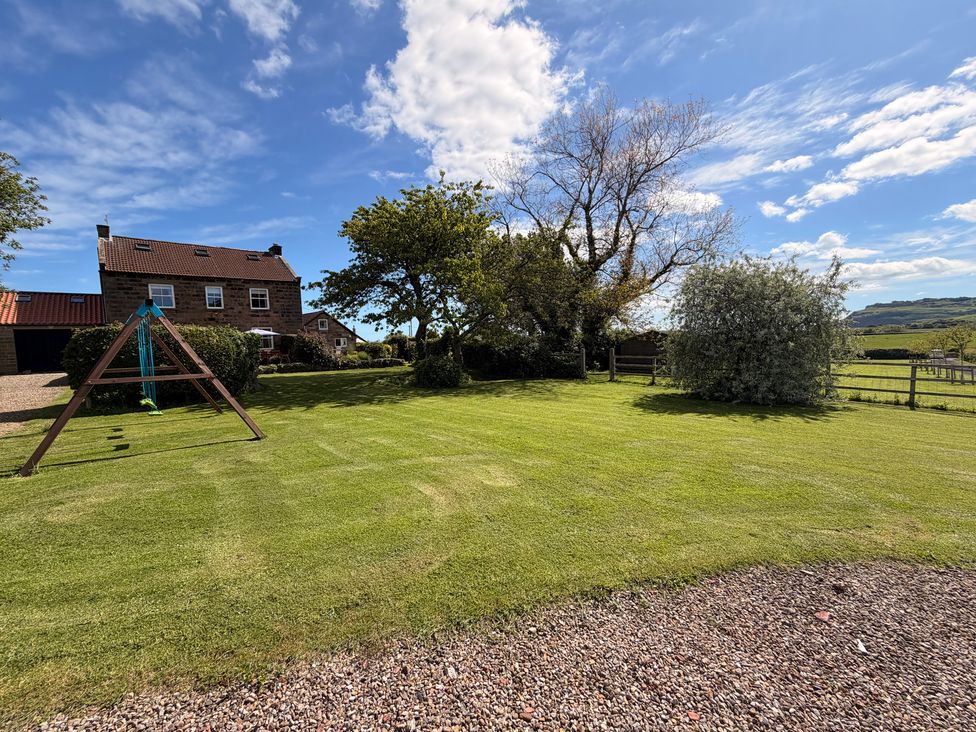 A garden with a swing set and trees at The Farmhouse in Boggle Hole near Robin Hood's Bay