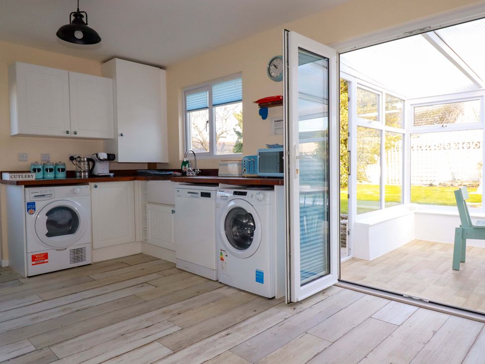 A kitchen with washing machines and a door leading to a conservatory at Merlin's Retreat in Tintagel
