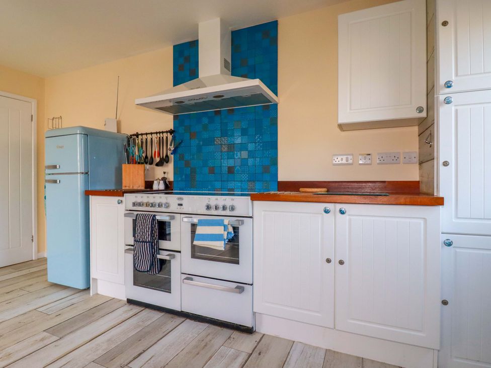 A kitchen with a blue fridge and white cabinets at Merlin's Retreat in Tintagel