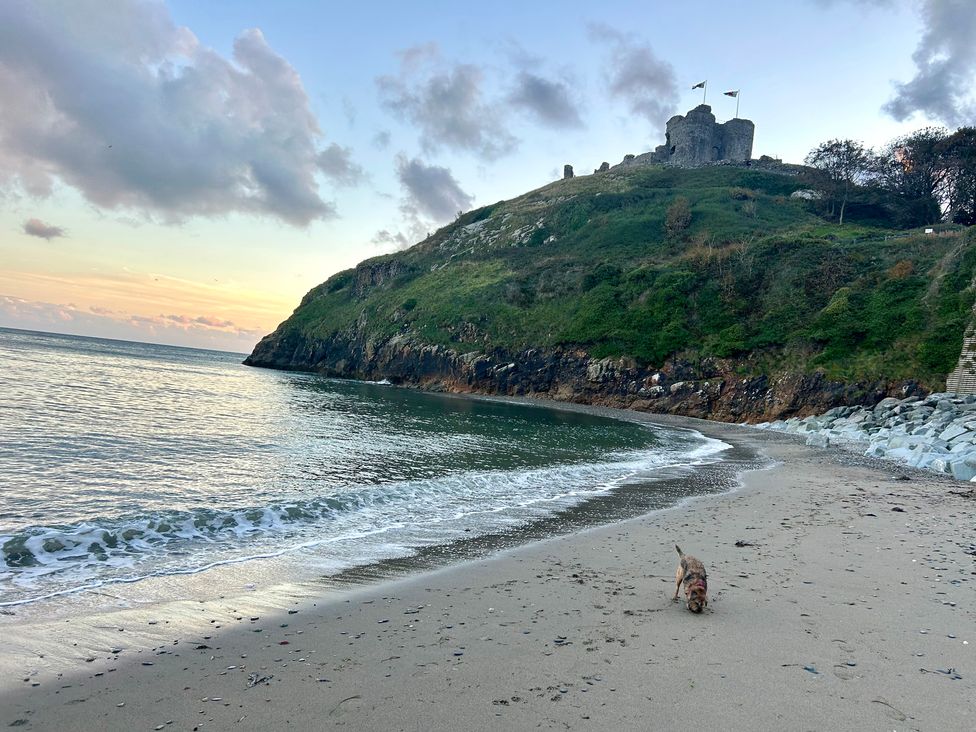 A beach with water and a castle on a hill at The View in Criccieth