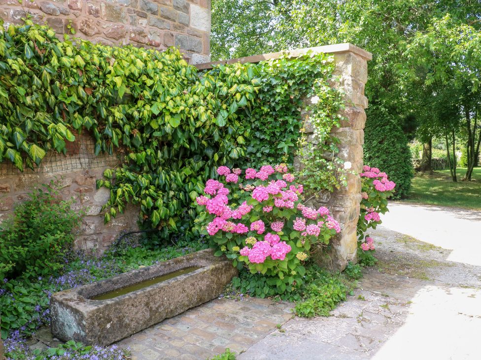 A garden with a stone wall, flowers, and an old water trough at Lee House Cottage in Cheddleton