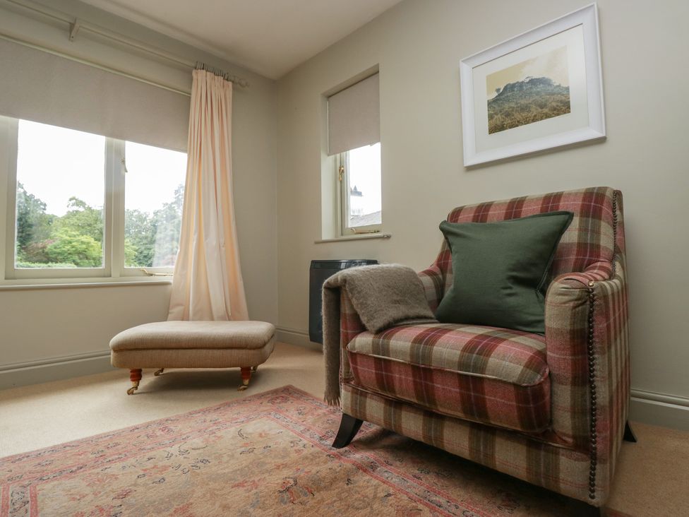 A snug area with a window, armchair, footstool and rug at Gable End in Coniston near Hawkshead