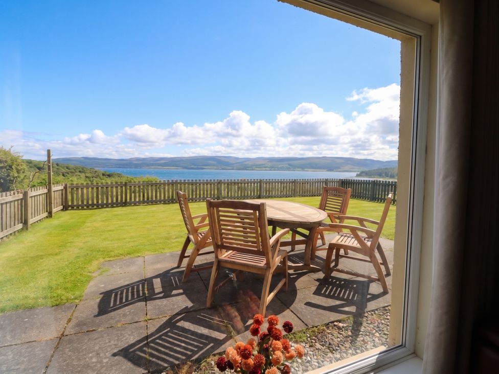 A patio with a table and chairs overlooking a view at Sunset Cottage in Craignure, Isle Of Mull