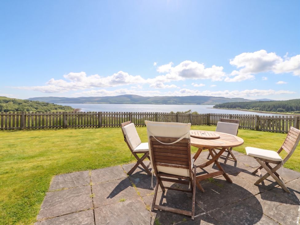 A patio with a table and chairs overlooking a lake at Driftwood Cottage, Craignure, Isle Of Mull