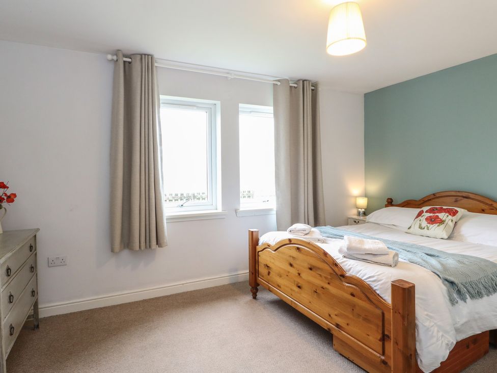 A bedroom with a double bed and windows at Poppies Cottage in Craignure, Isle Of Mull
